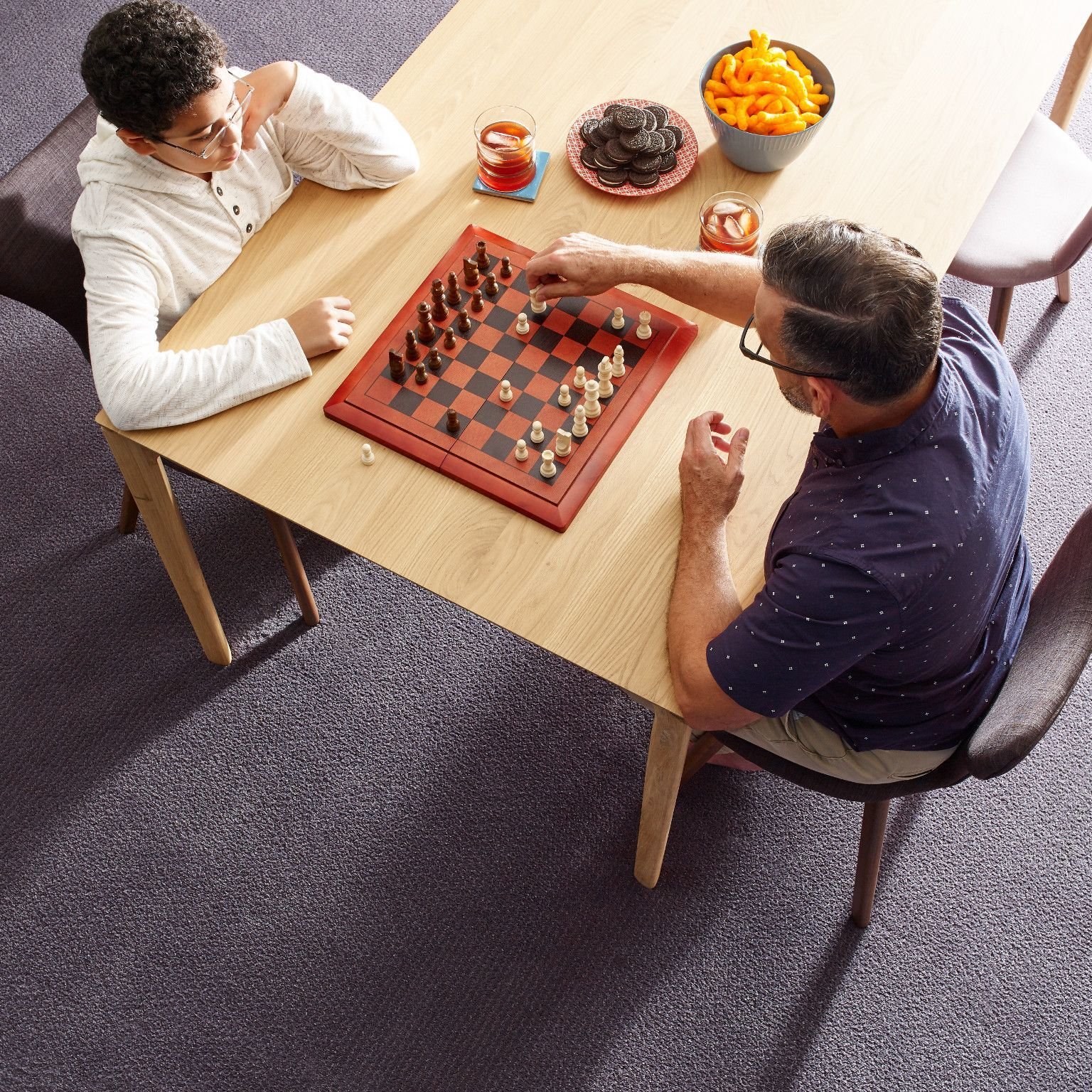 father and son playing chess and eating snacks in a living room with gray carpet by Fleeners Home Planning Inc in Leitchfield, KY